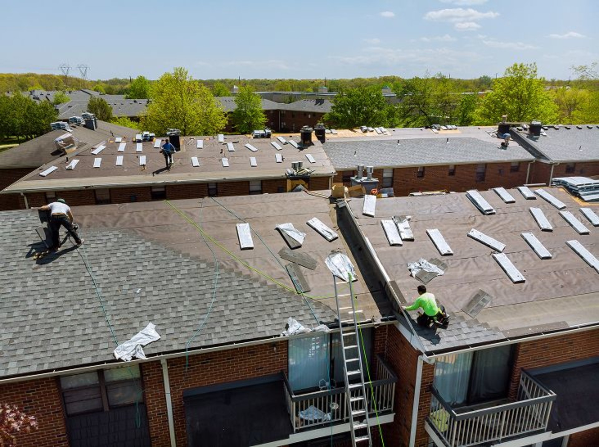 Roofers putting new shingles on a group of closely spaced residential buildings.